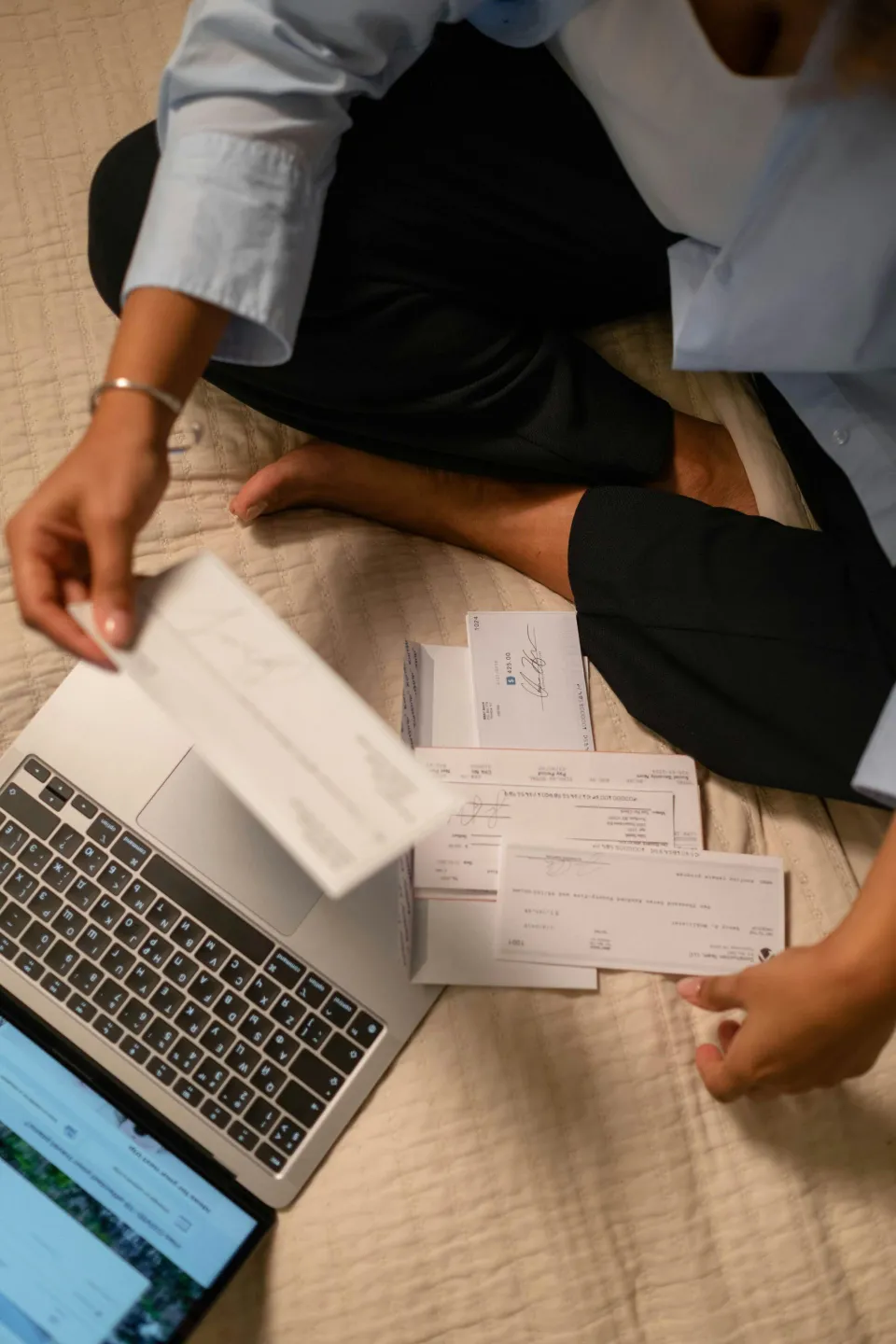 Hands sorting checks beside an open laptop.